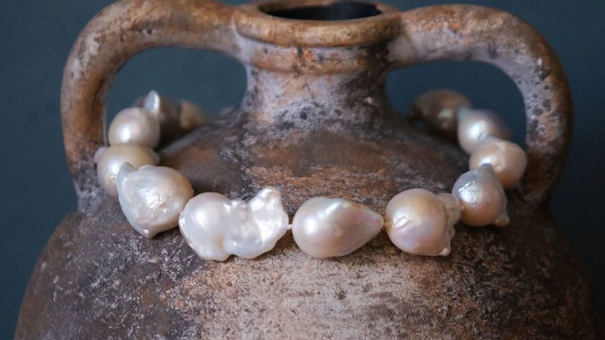 A necklace made of natural pearls displayed on a clay pot with a rustic finish.
