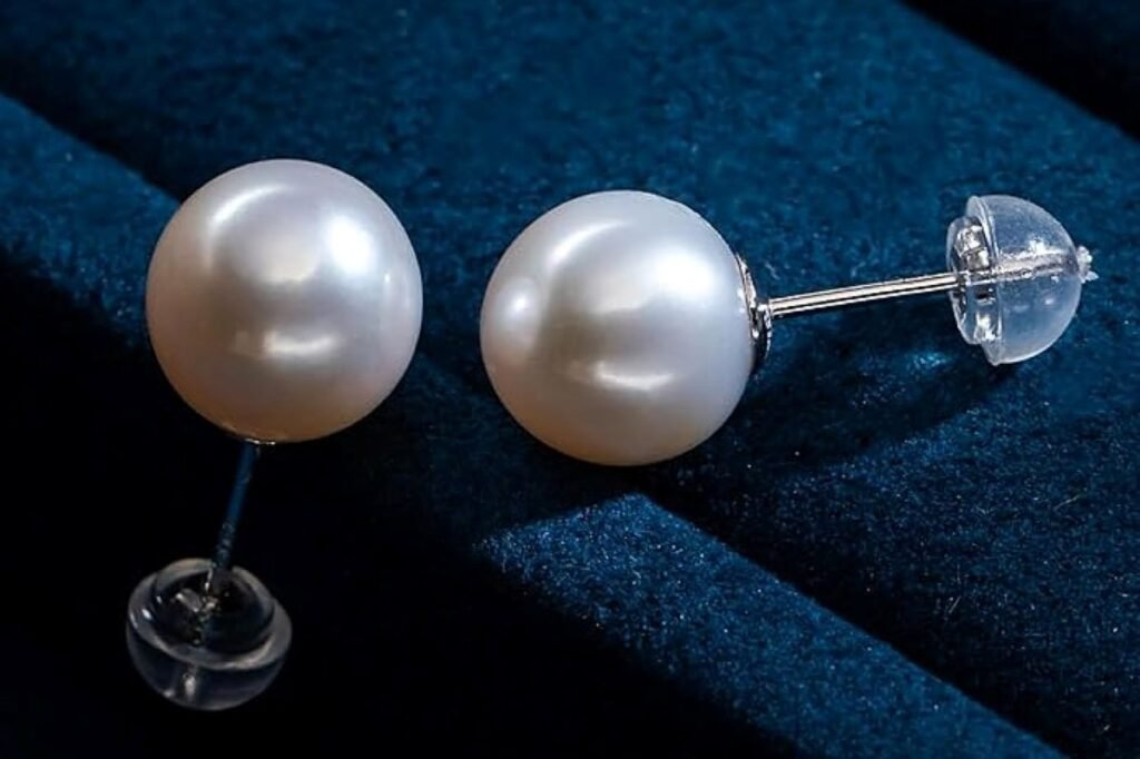 Natural freshwater pearl stud earrings with a round shape and silver posts, displayed on a dark velvet background.
