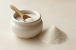 Small white ceramic bowl containing granulated sugar with a wooden spoon resting inside and a mound of sugar beside it.