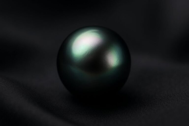 Tahitian pearl with a dark, iridescent surface resting on a smooth fabric background.