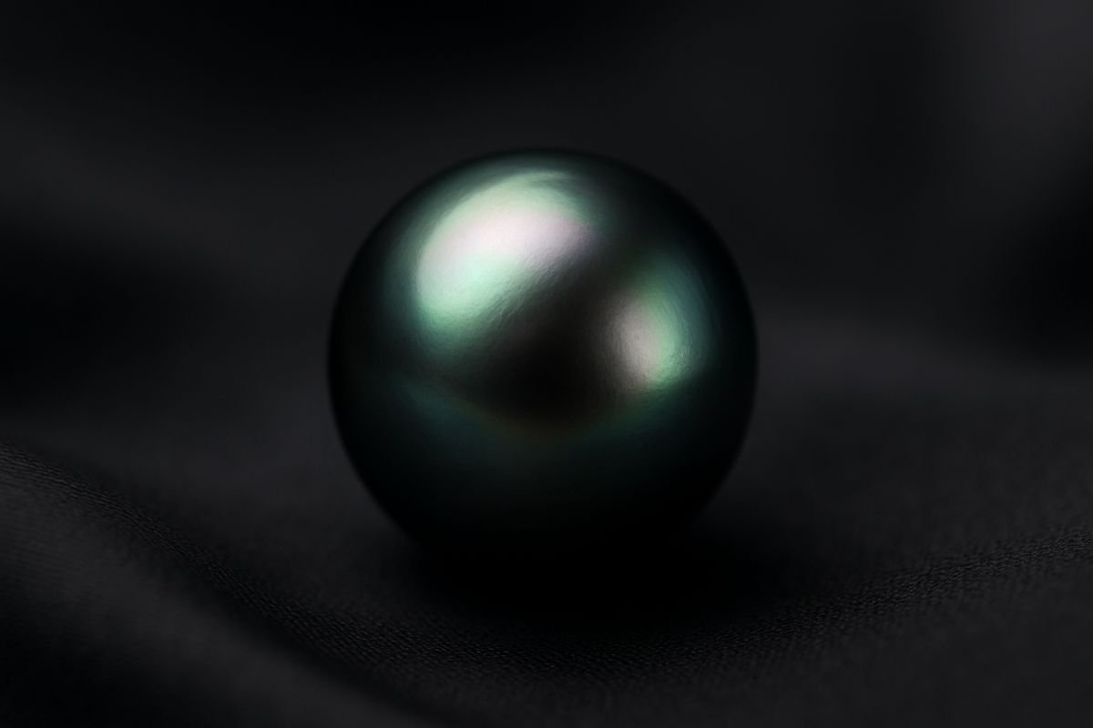 Tahitian pearl with a dark, iridescent surface resting on a smooth fabric background.