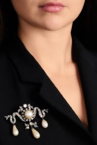 Ivory pearl-and-diamond brooch with a central round pearl and dangling pearl drops on black tailoring, echoing Princess Kunigunde of Saxony heritage.